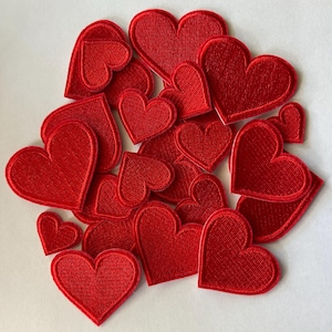 May include: A collection of red heart-shaped embroidered patches. The patches vary in size and are arranged on a white surface. The hearts have a textured appearance, with a stitched border. These patches are suitable for various craft projects.