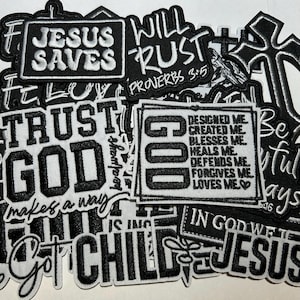 May include: A collection of black and white embroidered patches with religious phrases. The patches feature text like "Jesus Saves," "Trust God," and "God." The patches are in various shapes and sizes.