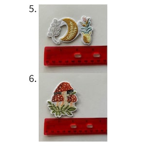 May include: Embroidered patches featuring celestial and botanical designs. One patch shows a crescent moon and sprig, another a potted plant. A third patch depicts a mushroom with red and white spots. A ruler is included for size reference.