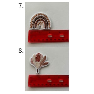 May include: Embroidered patches featuring a rainbow and a flower. The rainbow patch is in shades of brown and beige, approximately 2 inches wide. The flower patch is in shades of pink and brown, approximately 2 inches tall. Both patches have white borders.
