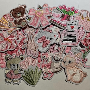 May include: A collection of embroidered patches in shades of pink, featuring various designs. The patches include teddy bears, ballet slippers, a typewriter with the word "I love you", a flamingo, and a bunny with a bow.