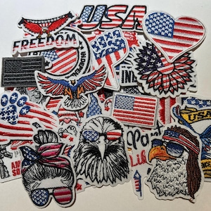 May include: A collection of patriotic patches featuring the American flag, eagles, and the word "Freedom." The patches are in red, white, and blue, with various shapes and designs, including a heart-shaped flag and a fist.