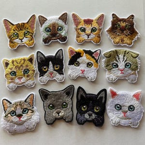 May include: A collection of twelve embroidered cat patches. Each patch features a different cat face with detailed stitching in various colors, including brown, black, white, and gray. The patches are designed with a variety of cat breeds and patterns.
