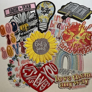 May include: A collection of embroidered patches with inspirational messages and floral designs. Includes patches with text like "Faith > Fear", "God is good", and "Love them anyway". Features a sunflower, rainbow, and heart-shaped patches.