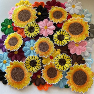 May include: A collection of embroidered flower patches in various colors, including yellow sunflowers, pink daisies, and blue flowers. The patches have detailed stitching and are arranged in a scattered pattern.