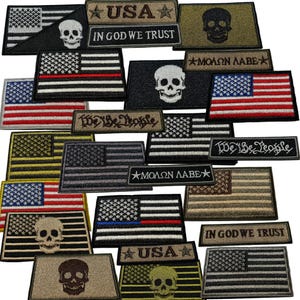 May include: A collection of embroidered patches featuring the American flag, skulls, and patriotic phrases. The patches display various color schemes, including black, white, red, blue, and tan. Some patches include the phrases "USA", "IN GOD WE TRUST", "We Be People", and "ΜΟΛΩΝ ΛΑΒΕ".