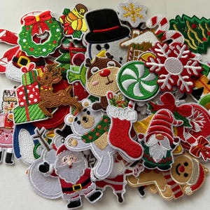 May include: A collection of Christmas-themed embroidered patches. The patches feature various festive designs, including Santa Claus, a snowman, reindeer, a Christmas tree, and a gingerbread man. The patches are in various colors, including red, green, white, and brown.