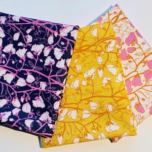 Könnte beinhalten: Drei Stoffquadrate mit einem floralen Muster. Die Stoffquadrate sind in den Farben Rosa, Gelb und Blau gehalten. Das Blumenmuster besteht aus weißen Blüten mit rosa, gelben und blauen Stielen.