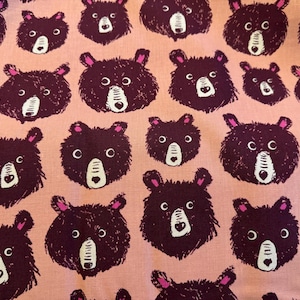 Könnte beinhalten: Ein rosa Stoff mit einem sich wiederholenden Muster aus braunen Bärenköpfen. Die Bären haben weiße Nasen und Augen.