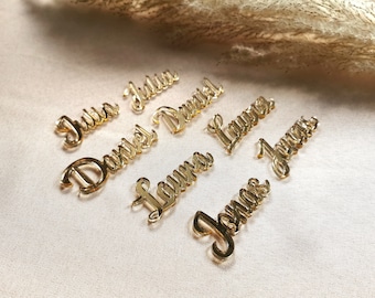 May include: Gold acrylic place cards with the names Julia, Daniel, Laura, and Jonas written in a cursive font.