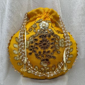 May include: A yellow drawstring bag with gold embroidery and pearl trim. The bag has a round shape and is decorated with a floral pattern.
