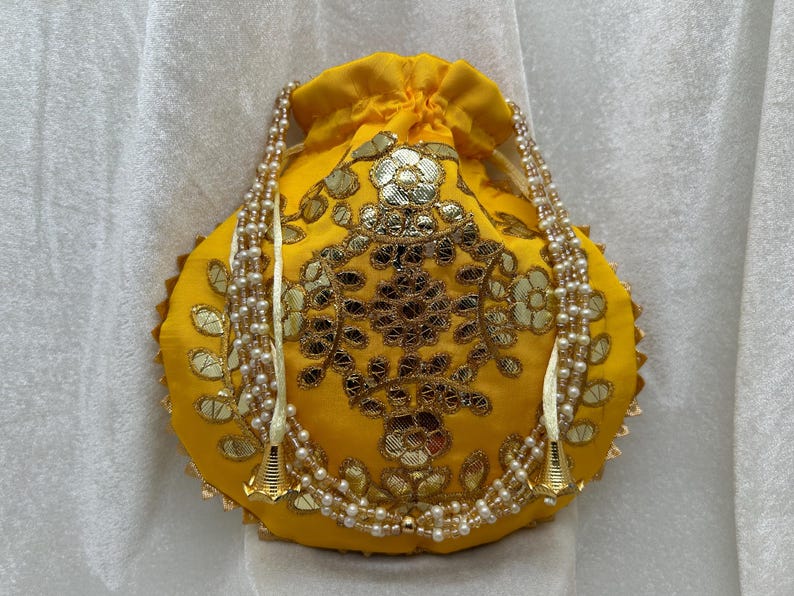 May include: A yellow drawstring bag with gold embroidery and pearl trim. The bag has a round shape and is decorated with a floral pattern.