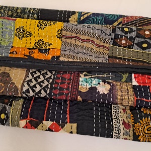 Op de afbeelding: Een veelkleurig patchwork-deken met een zwarte achtergrond. Het deken is gemaakt van verschillende stoffen met verschillende patronen, waaronder bloemen-, geometrische en paisley-patronen. Het deken is in drieën gevouwen en heeft een zwarte rand.
