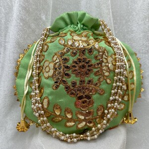 May include: A green drawstring bag with gold embroidery and a pearl and white string closure.