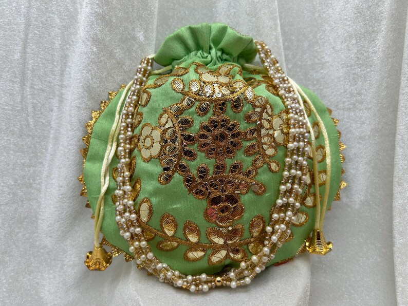 May include: A green drawstring bag with gold embroidery and a pearl and white string closure.