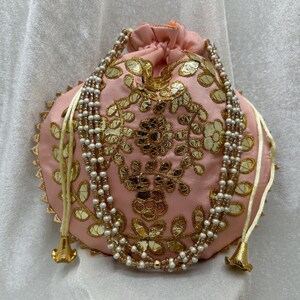 May include: A pink drawstring bag with gold and white embroidery and a pearl and gold beaded drawstring.
