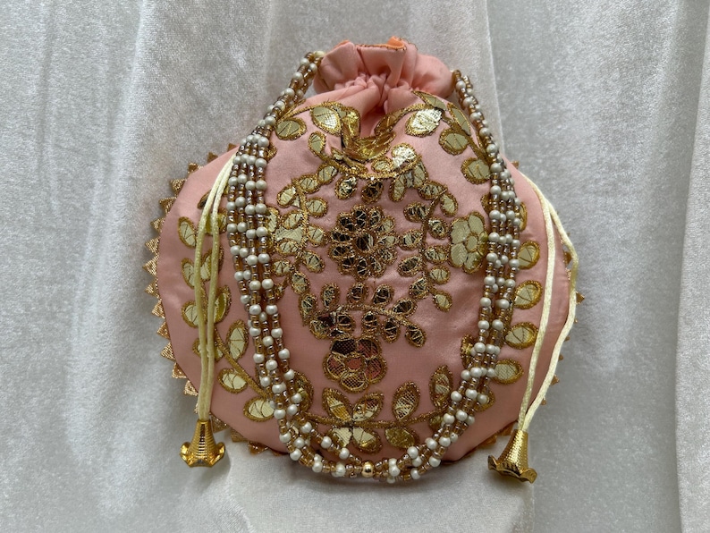 May include: A pink drawstring bag with gold and white embroidery and a pearl and gold beaded drawstring.