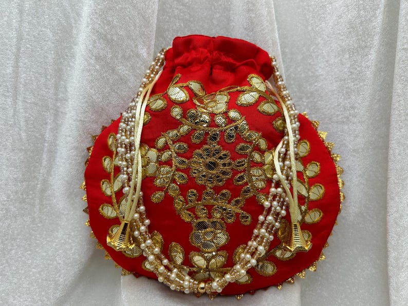 May include: A red drawstring bag with gold embroidery and white pearl beads. The bag has a scalloped edge and is decorated with floral patterns.