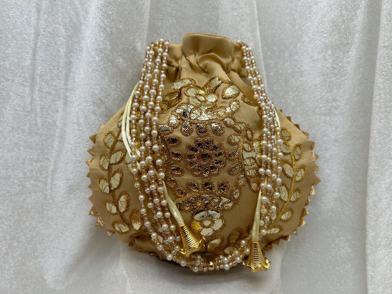 May include: A gold and cream drawstring bag with a floral design and pearl embellishments. The bag has a long, beaded strap.
