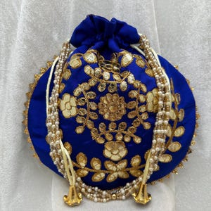 May include: A blue drawstring bag with gold embroidery and a white pearl trim. The bag has a round shape and is decorated with floral patterns.