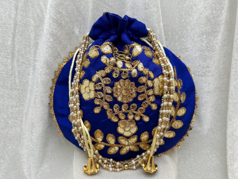 May include: A blue drawstring bag with gold embroidery and a white pearl trim. The bag has a round shape and is decorated with floral patterns.