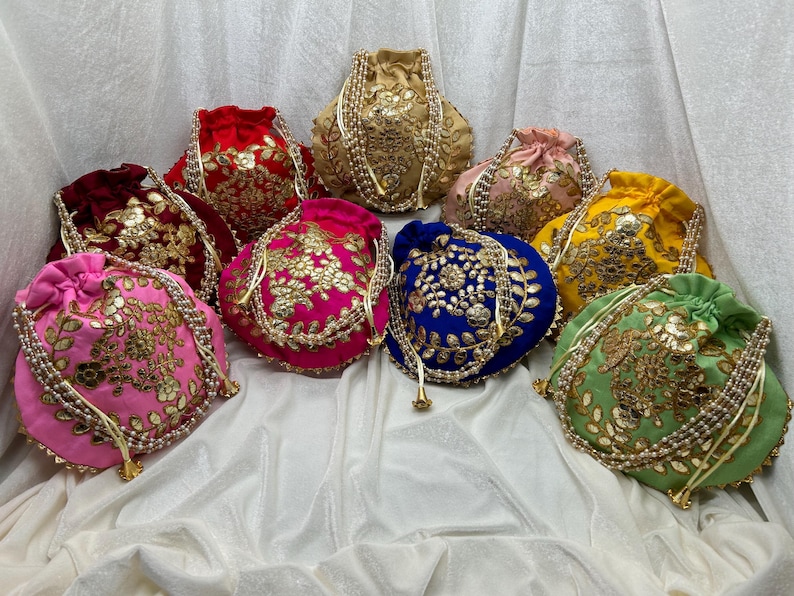 May include: Assortment of nine colorful drawstring bags with intricate embroidery and pearl embellishments. The bags are made of velvet and feature floral patterns in gold, silver, and other colors.