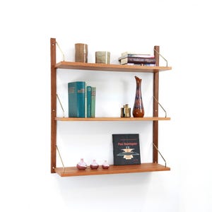 May include: A mid-century modern wall-mounted shelving unit with three wooden shelves. The shelves hold books, decorative vases, and small objects. The unit has brass supports and a dark wood frame, creating a stylish storage solution.