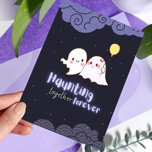 May include: A black card with a white and purple design featuring two cartoon ghosts holding a yellow balloon. The text "Haunting together forever" is written in a white and purple font.