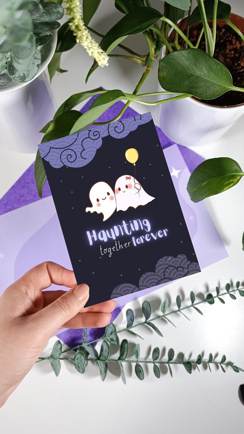 May include: A black card with a white ghost couple holding a yellow balloon. The card has a purple and white background with a repeating pattern of clouds. The text on the card reads "Haunting together forever."