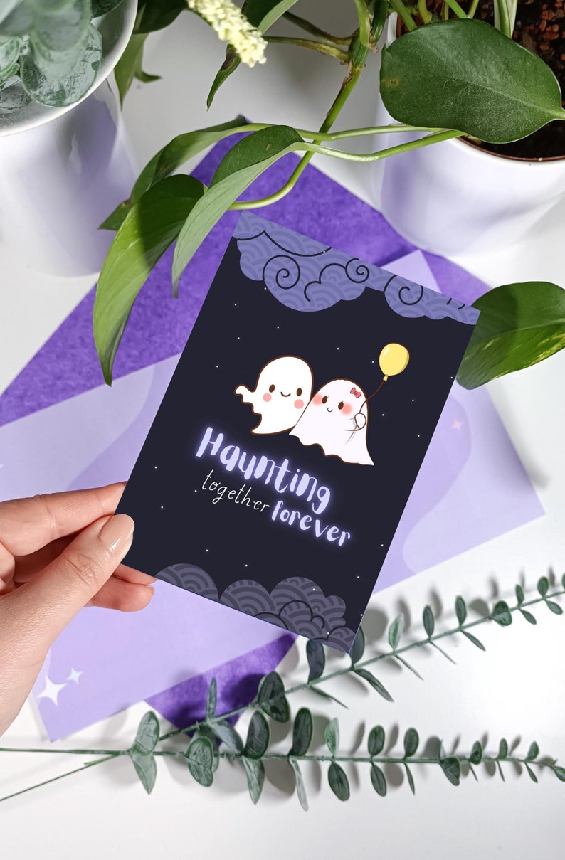 May include: A black card with a white and purple design featuring two cartoon ghosts holding a yellow balloon. The text "Haunting together forever" is written in a white and purple font.