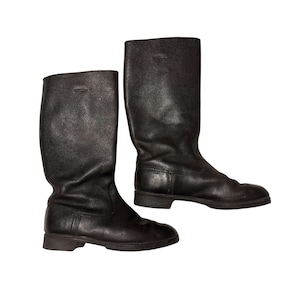 May include: A pair of black leather mid-calf boots featuring a textured grain finish, a rounded toe, and a low block heel. The boots have a tall, structured shaft with vertical stitching details near the heel and a simple, clean design throughout.