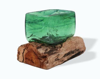 Puede incluir: Un cuenco de vidrio verde colocado sobre un trozo de madera a la deriva. El cuenco tiene una forma única y orgánica y está hecho de vidrio reciclado.