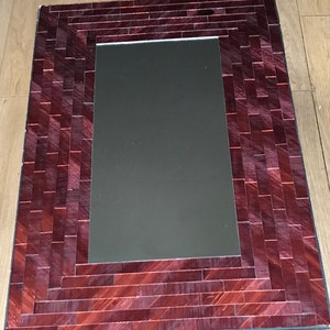 May include: A rectangular mirror with a decorative frame made of small, burgundy-coloured tiles. The tiles are arranged in a herringbone pattern.