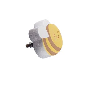 May include: A white wooden bee-shaped knob with a yellow and brown striped body and a smiling face. The knob has a silver screw for attaching to a drawer or cabinet.