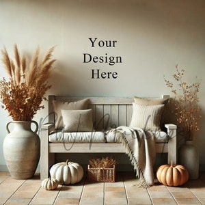 Puede incluir: Un banco de madera rústico con un acabado blanqueado, con dos almohadas y una manta. El banco está decorado con hierba de la pampa seca, una cesta de mimbre y dos calabazas. El texto "Your Design Here" está escrito en la pared detrás del banco.