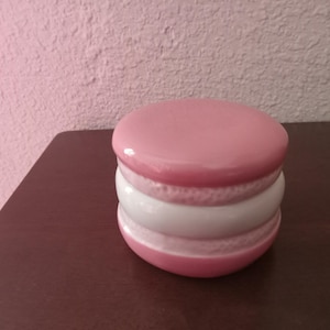 May include: A pink and white ceramic macaron shaped trinket box. The box has a smooth, glossy finish.