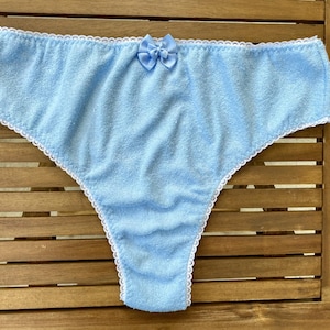 Könnte beinhalten: Hellblaue Frottee-Unterwäsche mit weißer Spitzenborte und einer hellblauen Schleife aus Satin.