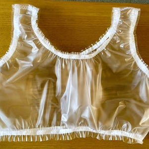 May include: A clear plastic top with a ruffled trim. The top is sleeveless and has a scoop neck.