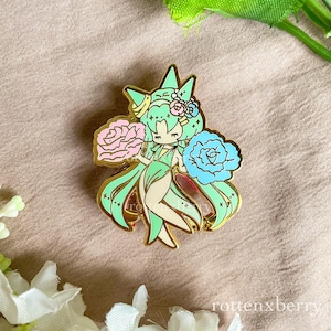 May include: A gold-colored enamel pin featuring a stylized anime-style character with mint green hair and a flowing green dress. The character holds a pink and a blue rose. The pin has a gold border and the text "rottenxberry" is visible.