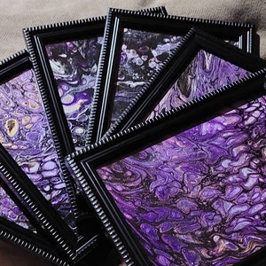 May include: A set of framed abstract paintings with purple, gold, and black swirling patterns. The frames are black with a decorative border.