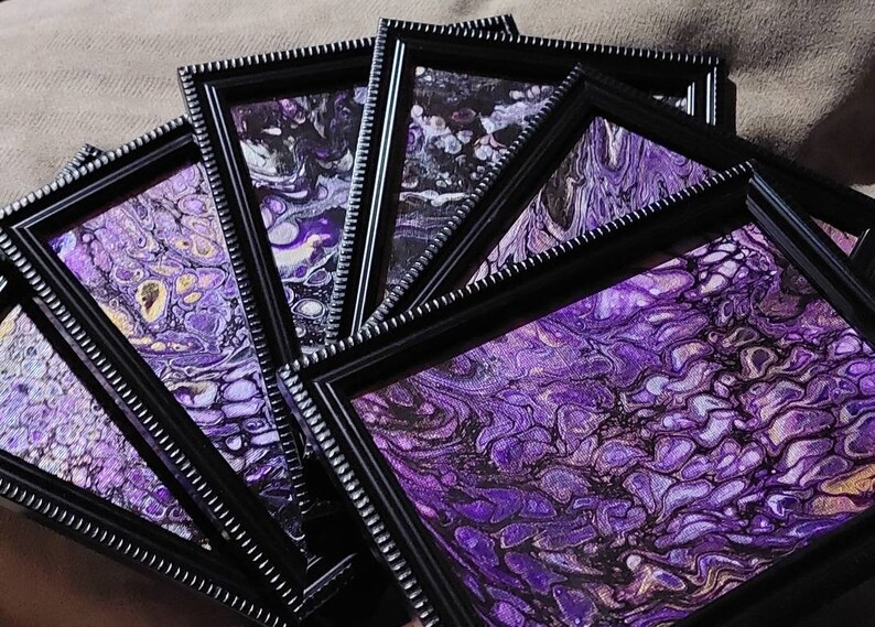 May include: A set of framed abstract paintings with purple, gold, and black swirling patterns. The frames are black with a decorative border.