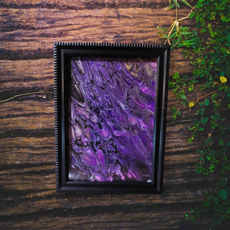 May include: A framed abstract painting with swirling purple and black paint. The painting is in a black frame with a white border.
