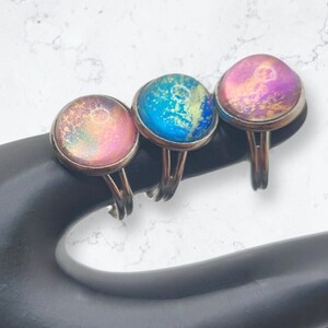 May include: Three silver rings with colorful resin insets. The rings feature a pink, blue, and purple resin with gold flecks.