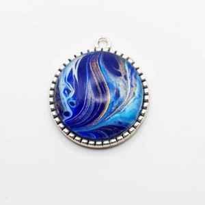 May include: A silver pendant with a blue, white, and gold marbled design. The pendant is round and has a silver border.