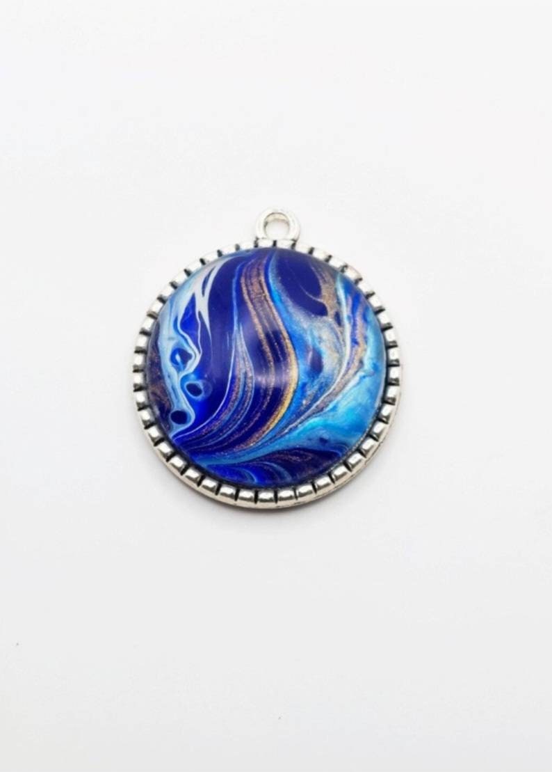 May include: A silver pendant with a blue, white, and gold marbled design. The pendant is round and has a silver border.