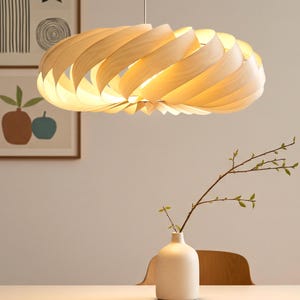 Pode incluir: Uma moderna luminária pendente de madeira, com um design em espiral. A luz é feita de madeira clara e emite um brilho quente. A luminária é suspensa do teto, iluminando o espaço abaixo. A luminária é um elemento decorativo.