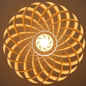 Op de afbeelding: Een moderne, geometrische lamp met een warme, uitnodigende gloed. De lamp heeft een spiraalvormig ontwerp van houten latten, waardoor een uniek, opvallend patroon ontstaat. De lichtbron is een heldere, centrale lamp.