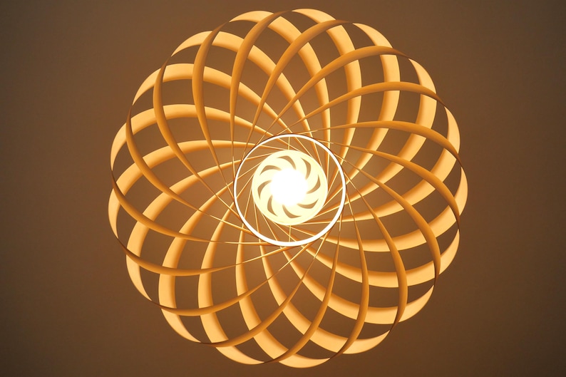 Op de afbeelding: Een moderne, geometrische lamp met een warme, uitnodigende gloed. De lamp heeft een spiraalvormig ontwerp van houten latten, waardoor een uniek, opvallend patroon ontstaat. De lichtbron is een heldere, centrale lamp.