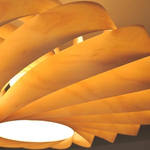 Op de afbeelding: Een moderne houten hanglamp met een spiraalvormig ontwerp. Het licht is gemaakt van gelaagde, gebogen houten panelen in tinten lichtbruin en geel, met een helder wit licht dat uit het midden komt.