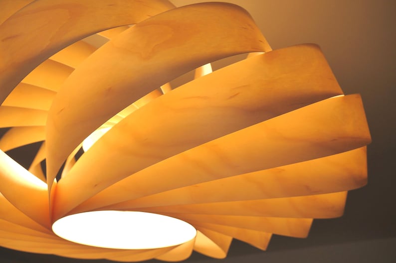Op de afbeelding: Een moderne houten hanglamp met een spiraalvormig ontwerp. Het licht is gemaakt van gelaagde, gebogen houten panelen in tinten lichtbruin en geel, met een helder wit licht dat uit het midden komt.